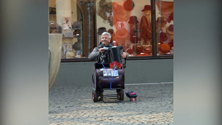 Älterer Herr sitzt in der Fußgängerzone und spielt Akkordeon