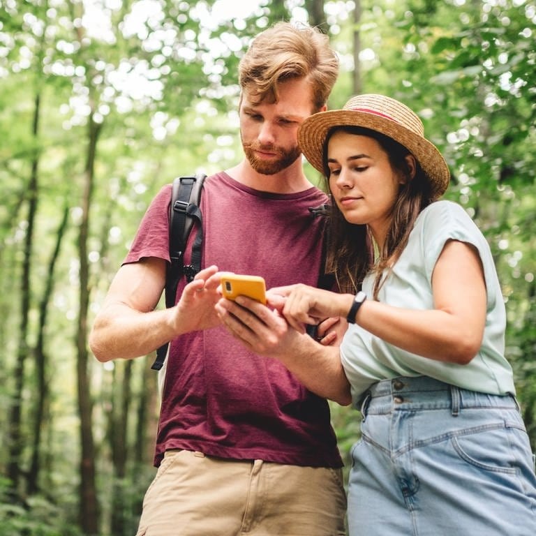 Kostenlose Wander-App: Junger Mann und junge Frau schauen im Wald auf ein Smartphone