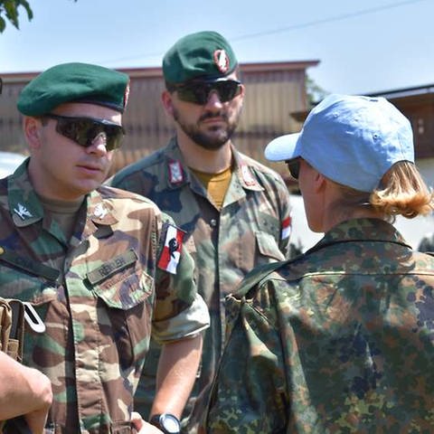 Eine Frau und drei Männer in Soldatenuniformen reden miteinander