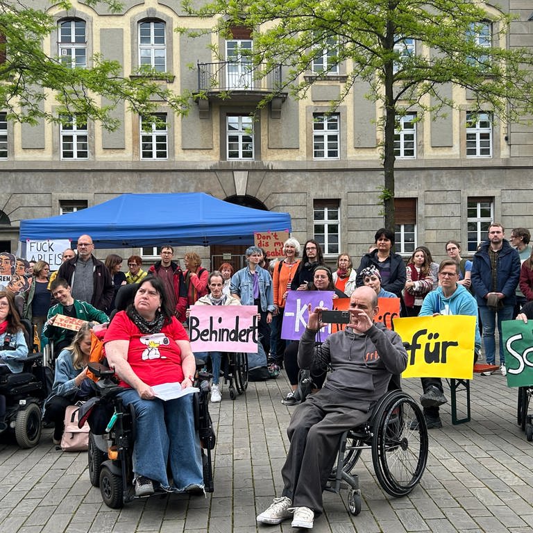 Menschen mit Rollstühlen und ohne haben sich in Heidelberg versammelt. Sie halten Banner und protestieren für mehr Inklusion.
